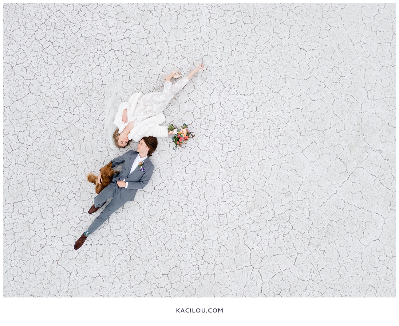 Bride and groom lying on ground with dog at salt flats white ground
